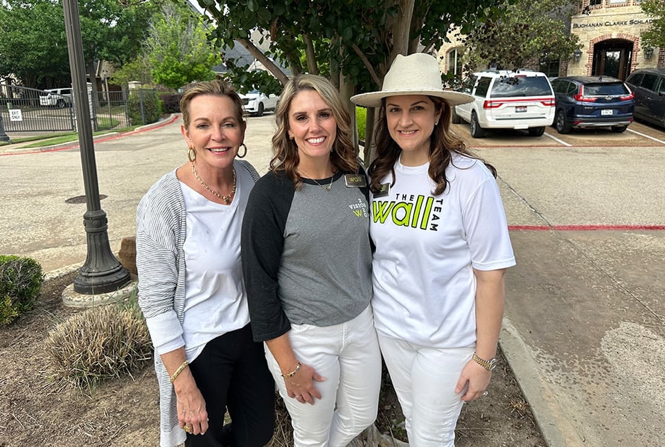 Three ladies with a tree and cars parked in the background