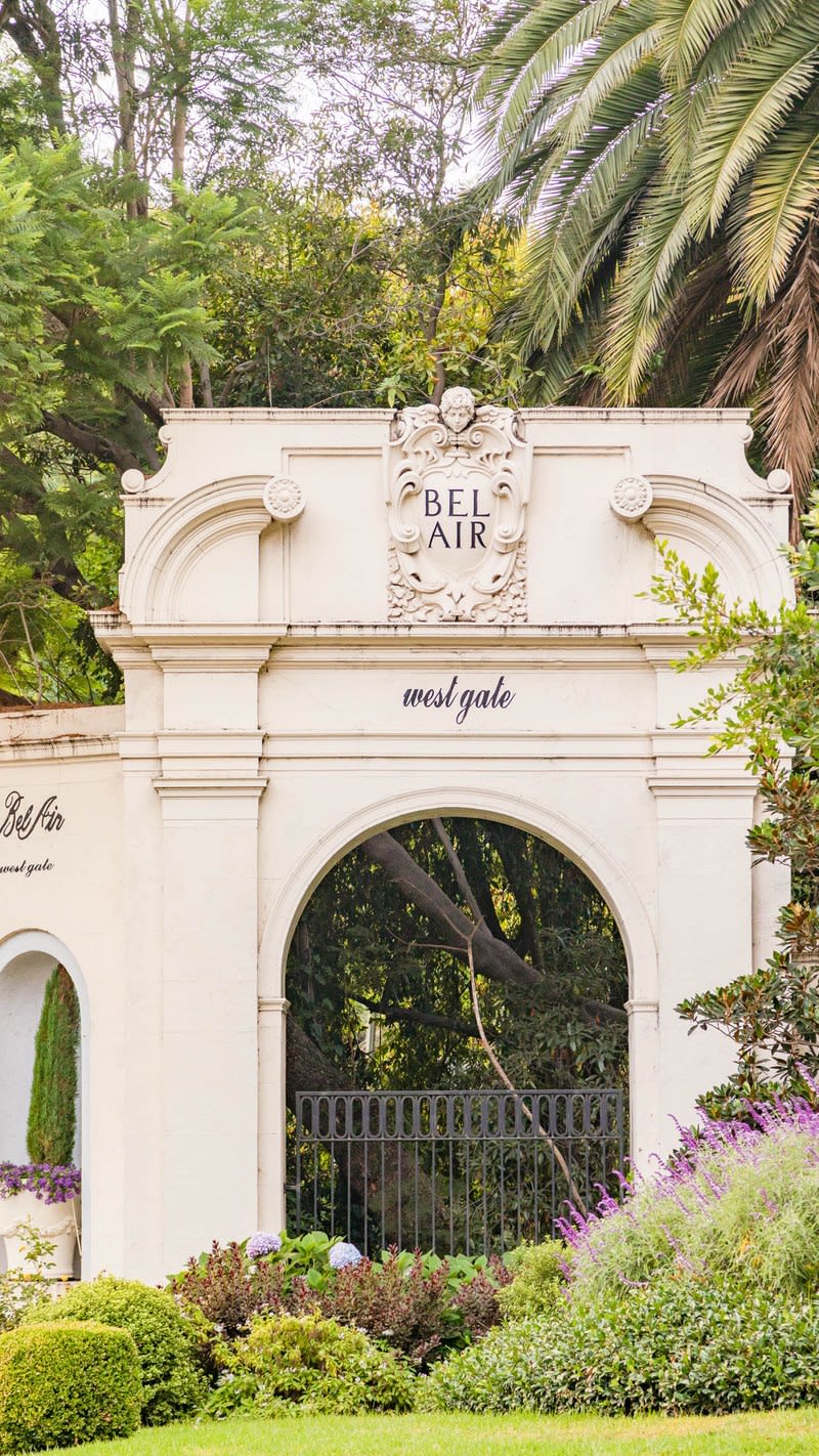 An archway is surrounded by trees and flowers, leading into a garden