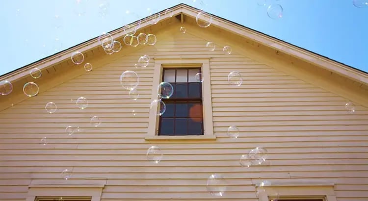A house with bubbles floating around it, creating a whimsical and playful atmosphere. The house is painted a light color, possibly yellow.