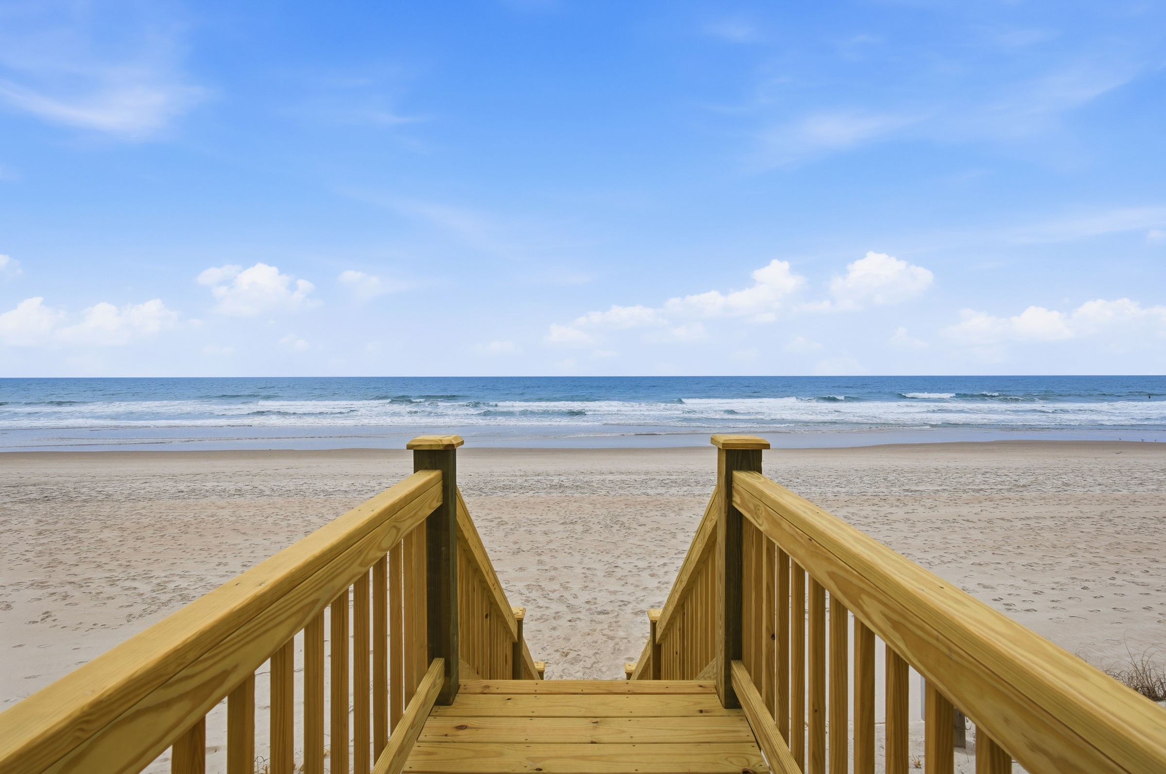 Wooden stairs lead across the sandy beach toward the ocean.