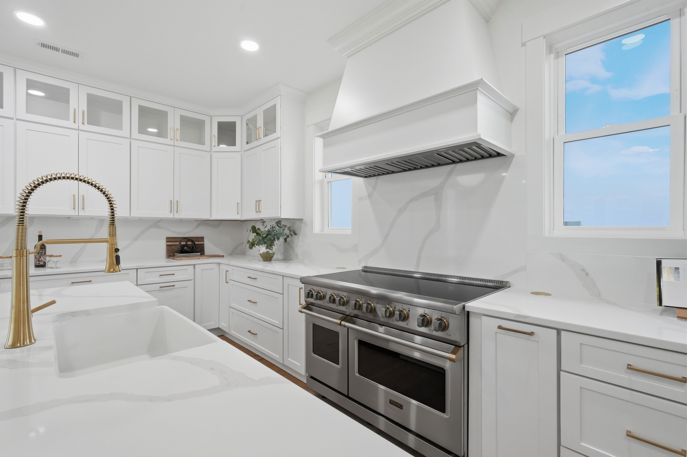 White kitchen with a large stainless-steel range, veined marble surfaces, and brass faucet.