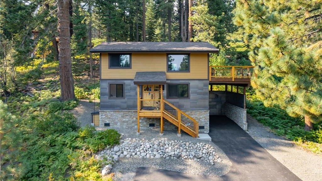 Two-story home with mustard-yellow and gray siding, a stone base, a covered wood entry stair and a deck, among tall pines and ferns at 786 Randall Avenue in the Jennifer neighborhood, Incline Village