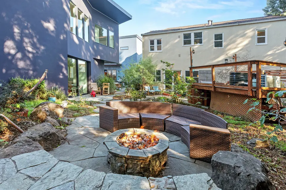 Shared courtyard with a circular fire pit, curved seating, and a raised wooden deck between residential buildings.