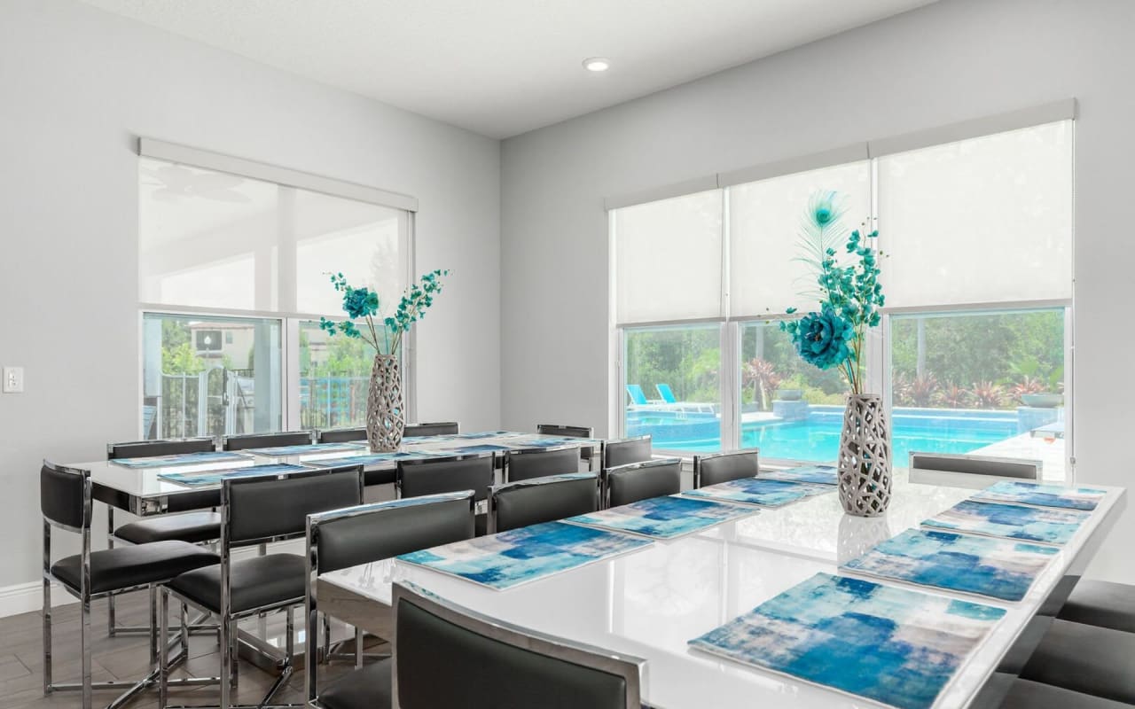 A bright and spacious dining room with a view of a swimming pool and a patio through large windows.