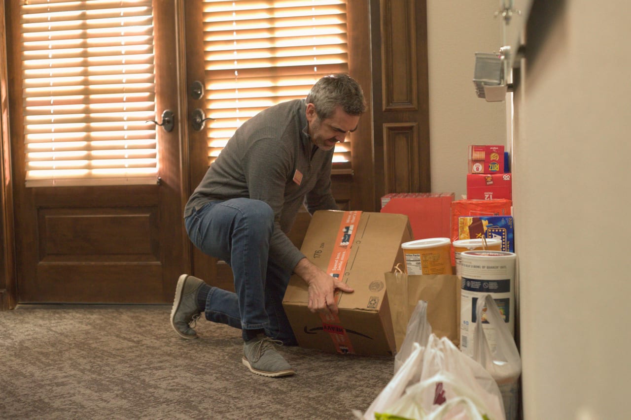 A man holding a box of groceries with a brown double door in the background