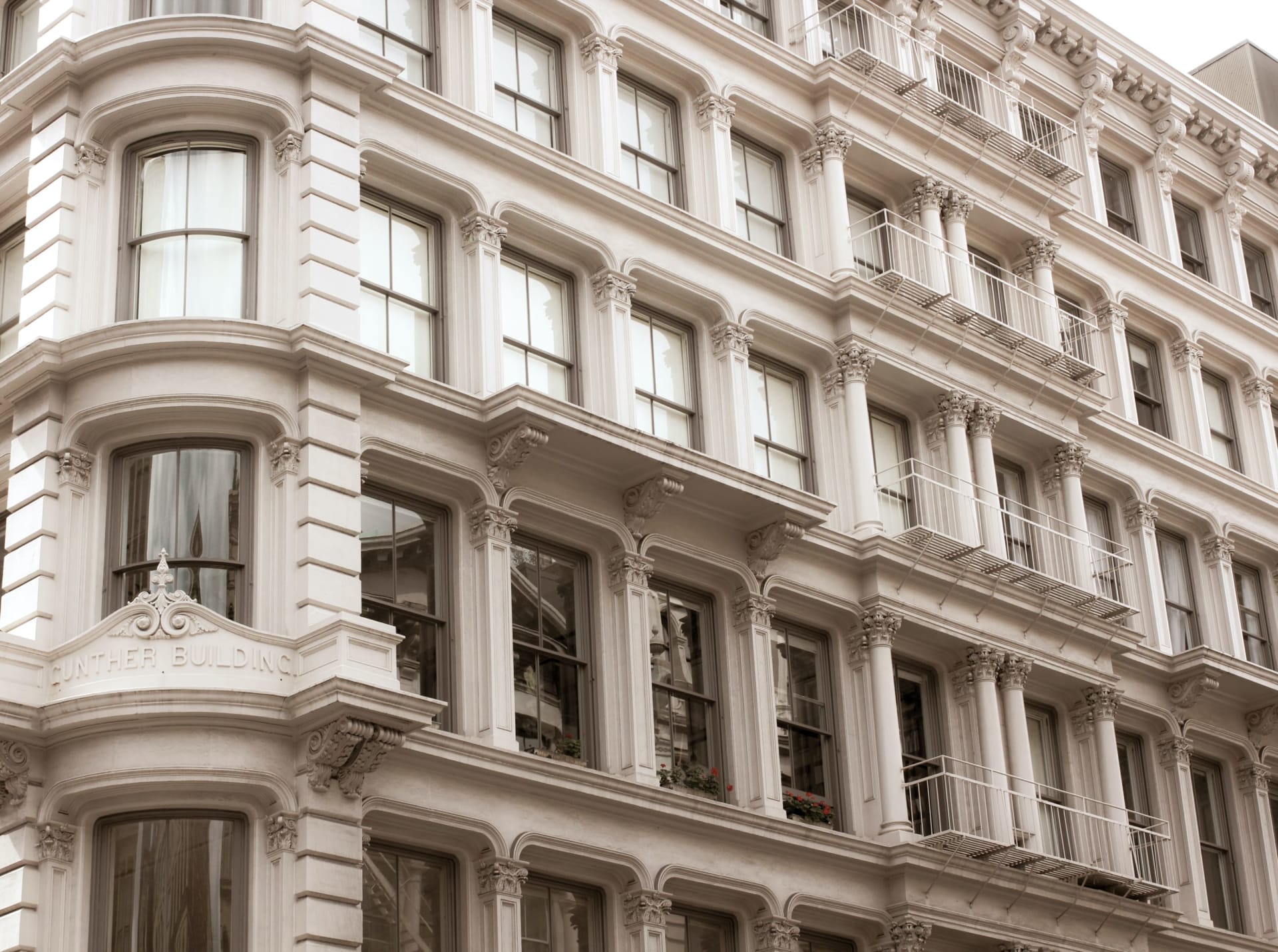 The Gunther Building’s ornate pale facade with decorative columns, curved bays, and metal fire escapes.