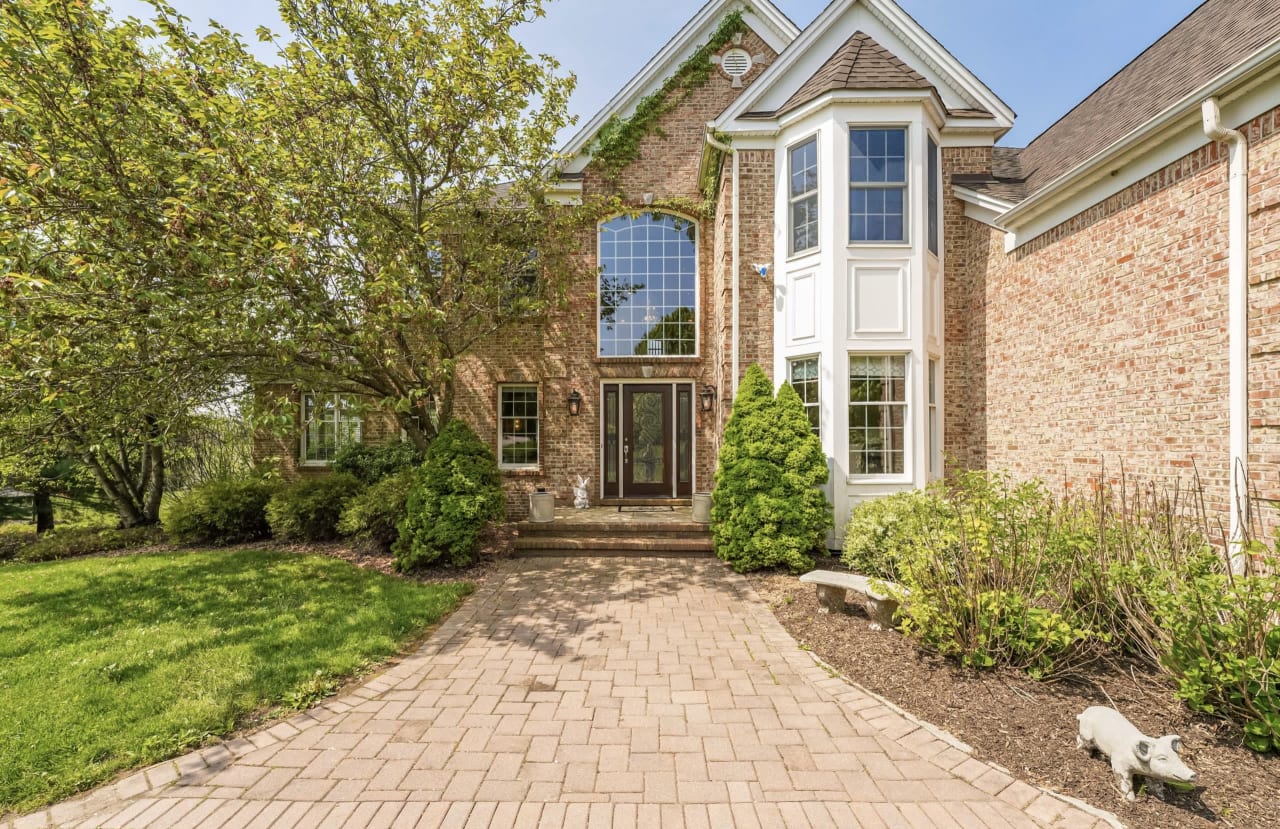 Exterior of a brick house with large windows, a paved driveway, and lush greenery surrounding the entrance.