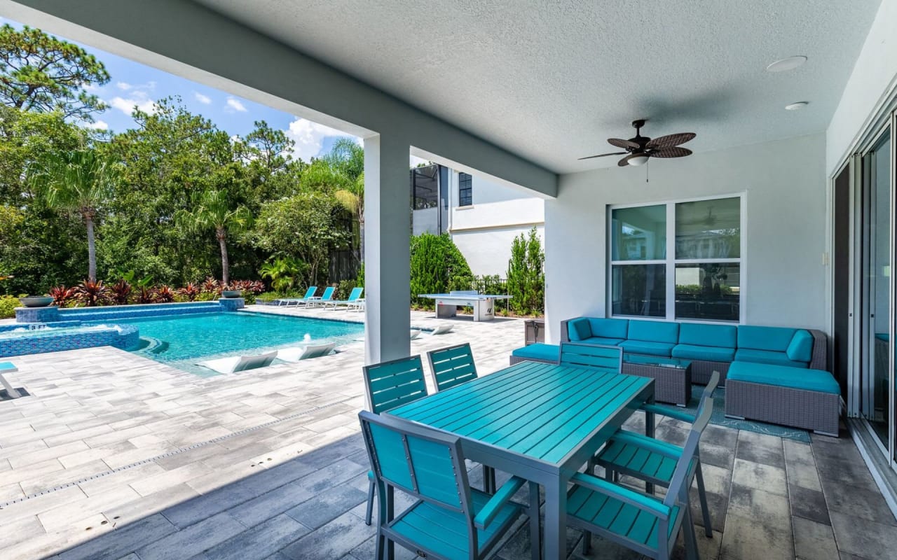 A patio with a table and four chairs next to a rectangular pool with blue tile lining.