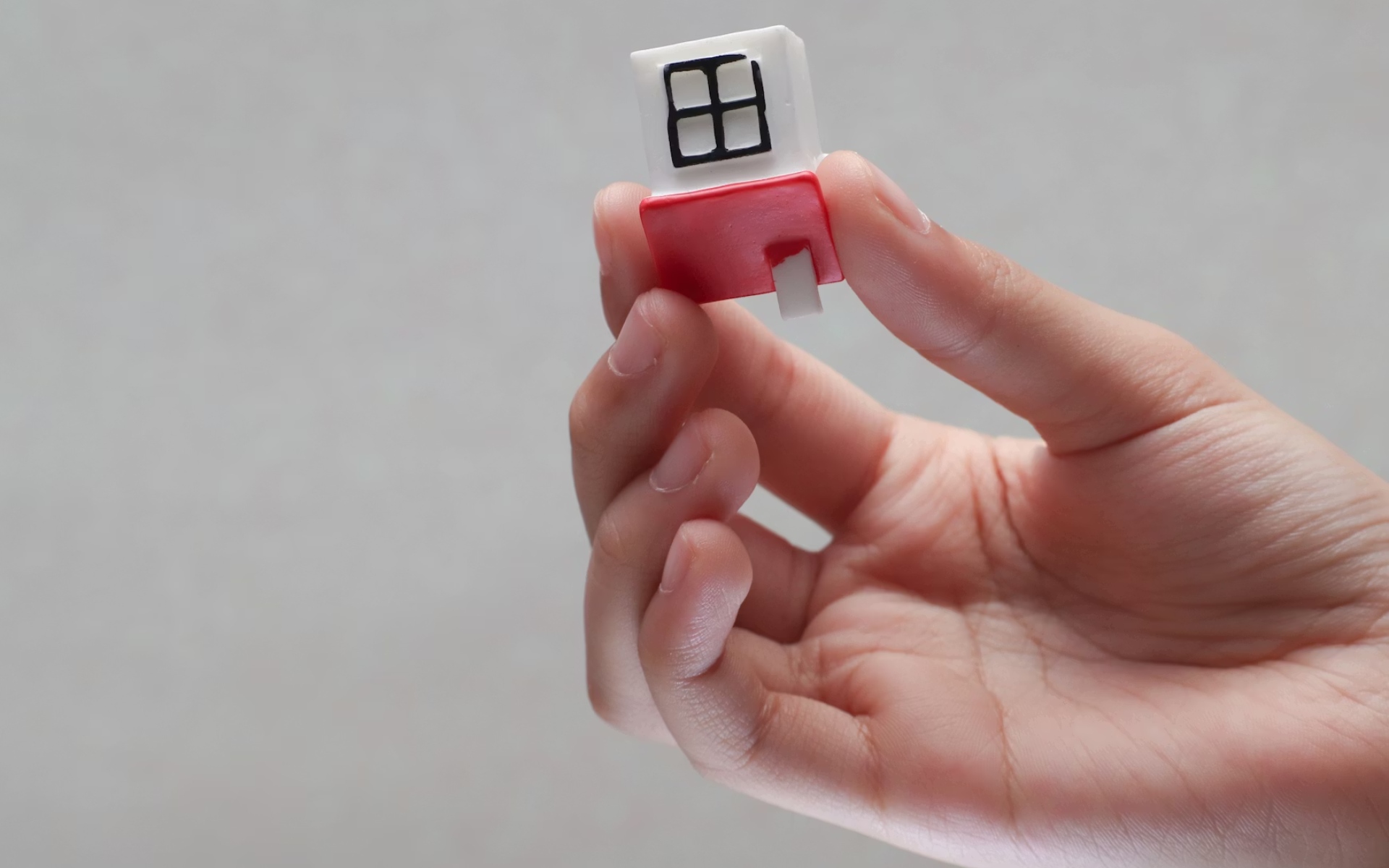 Hand Holding a Small Toy House Featuring a White Roof and Black Windows