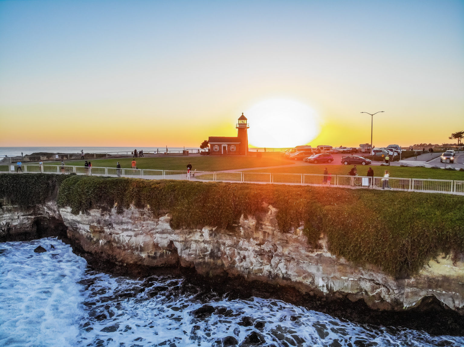 Santa Cruz coastal lighthouse at sunset above rocky cliffs and waves.
