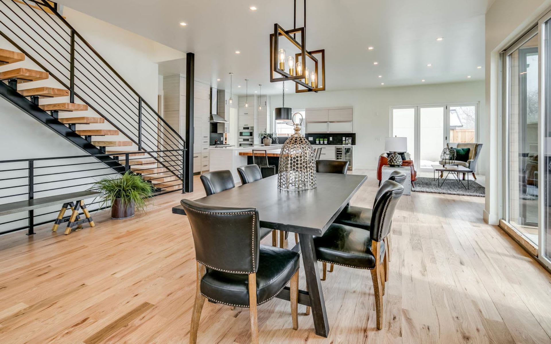 a dark gray dining table is surrounded by six black leather dining chairs with visible nailhead trim.