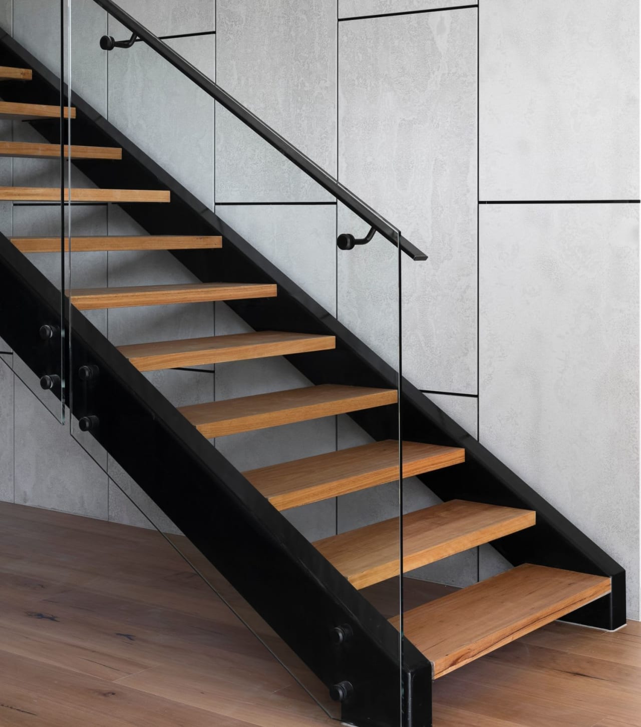 A modern staircase with light colored wooden steps and a clear glass railing.