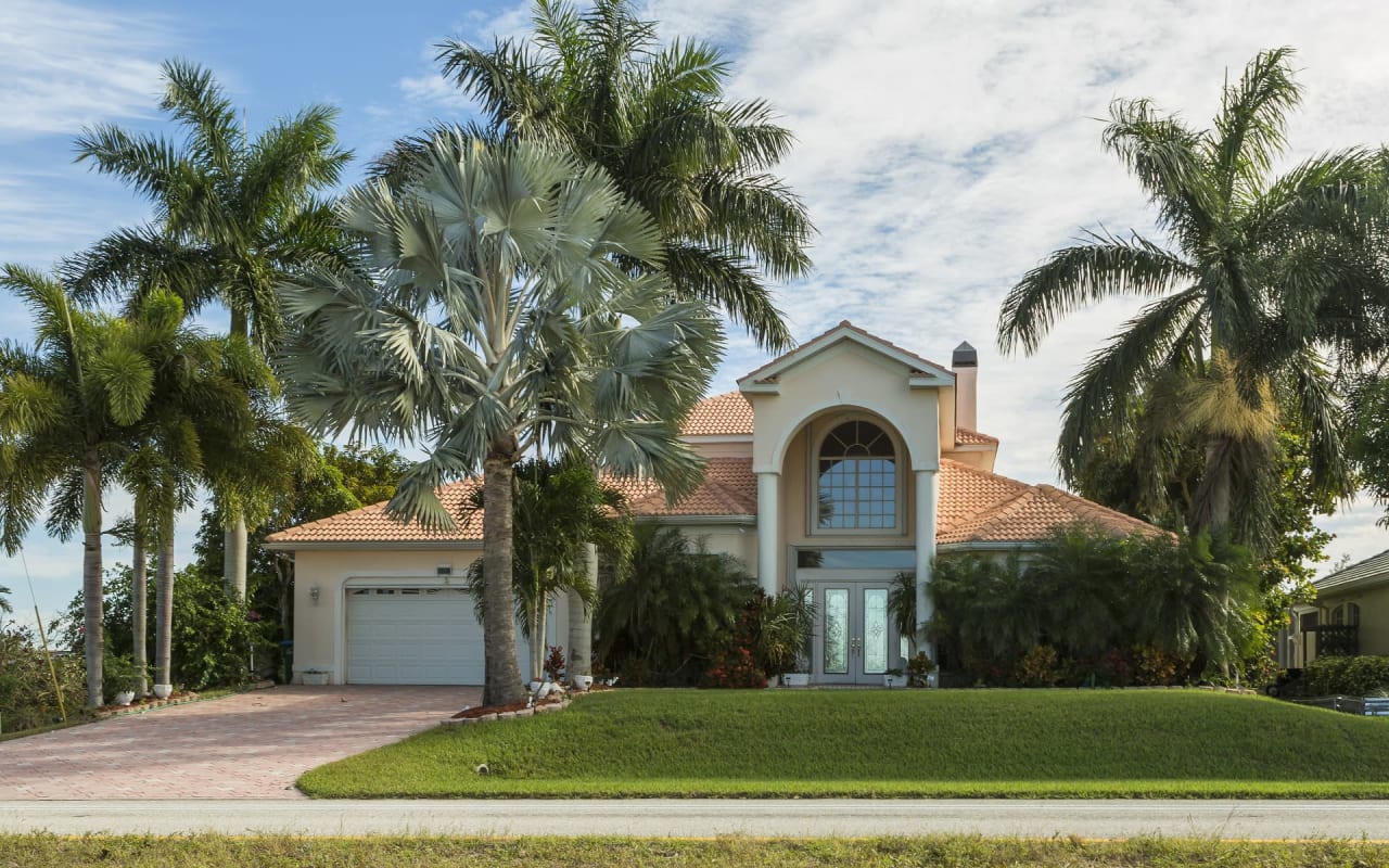 A single-family home with a car garage, a red brick walkway leading to the front door, and lush green landscaping.