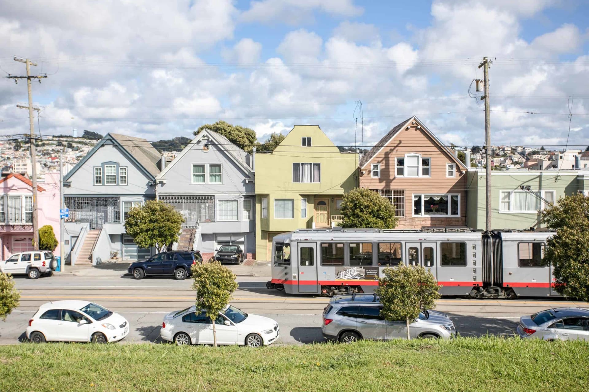 Colorful San Francisco homes behind a passing light-rail train, with hillside houses in the background.
