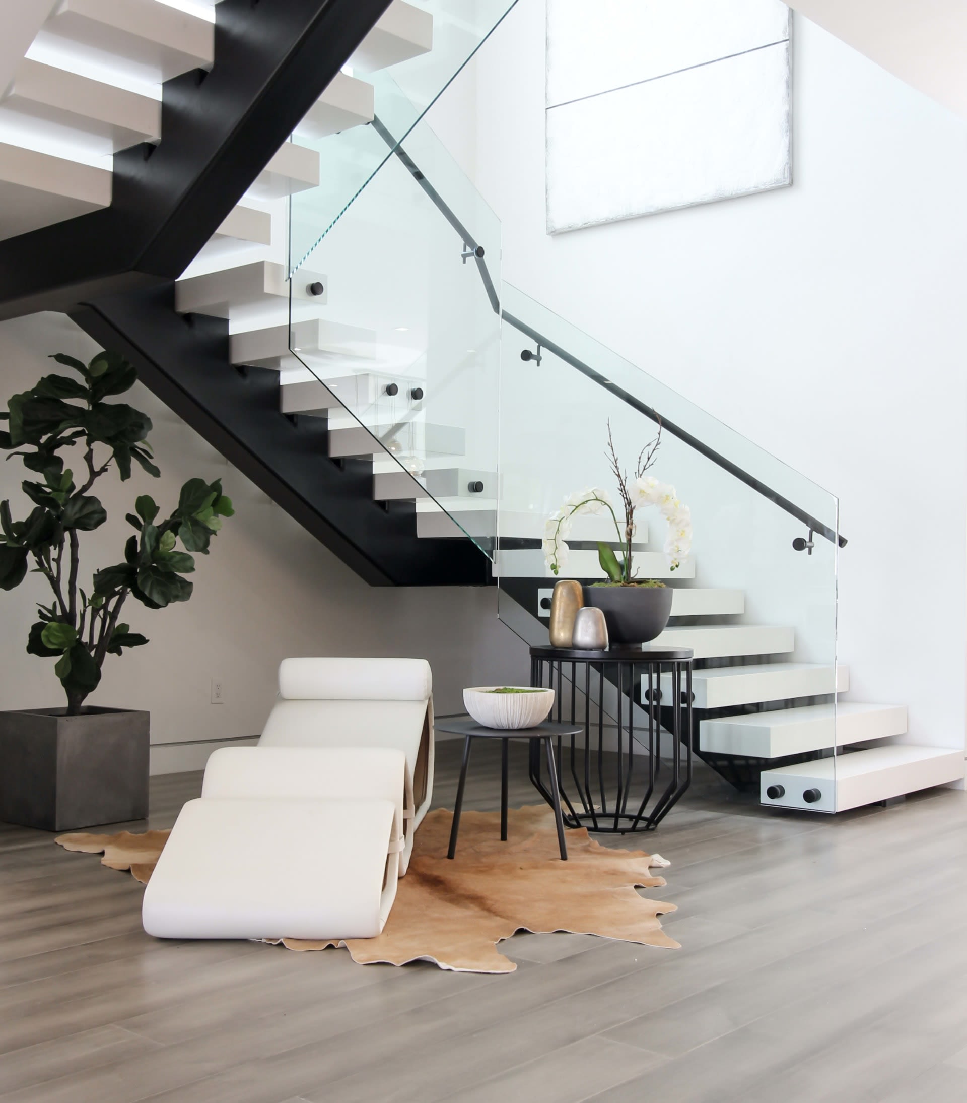 Modern interior with a floating white staircase, glass railing, and white lounge chair.