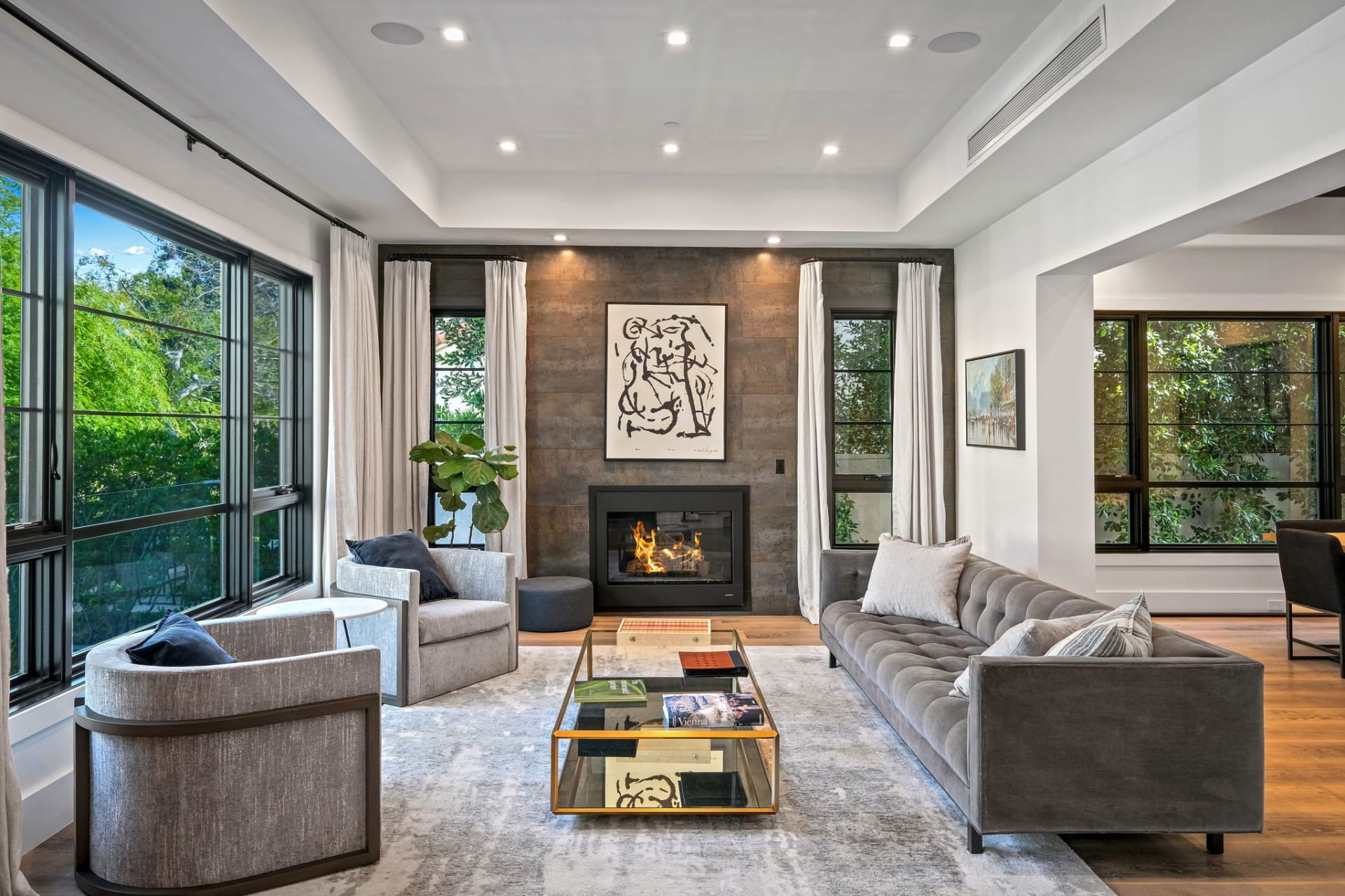  A luxurious and spacious modern living room features a long gray tufted sofa on the right and two matching gray armchairs 