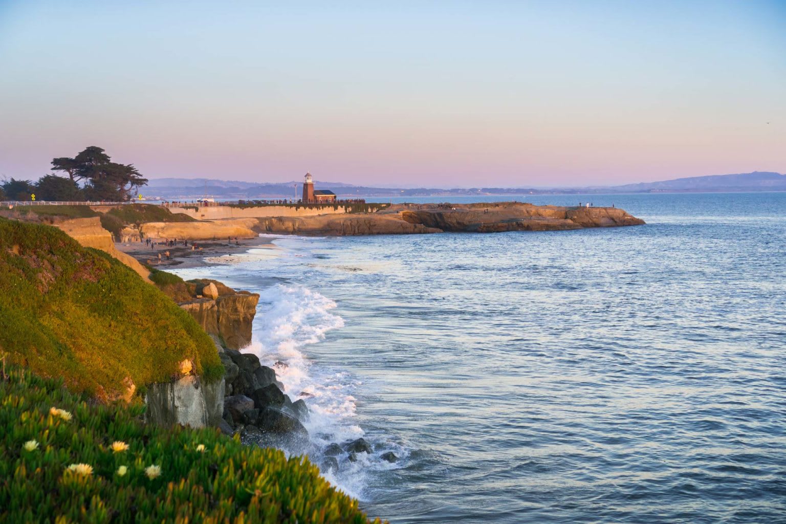 Rocky ocean shoreline with a small lighthouse on a point at golden hour
