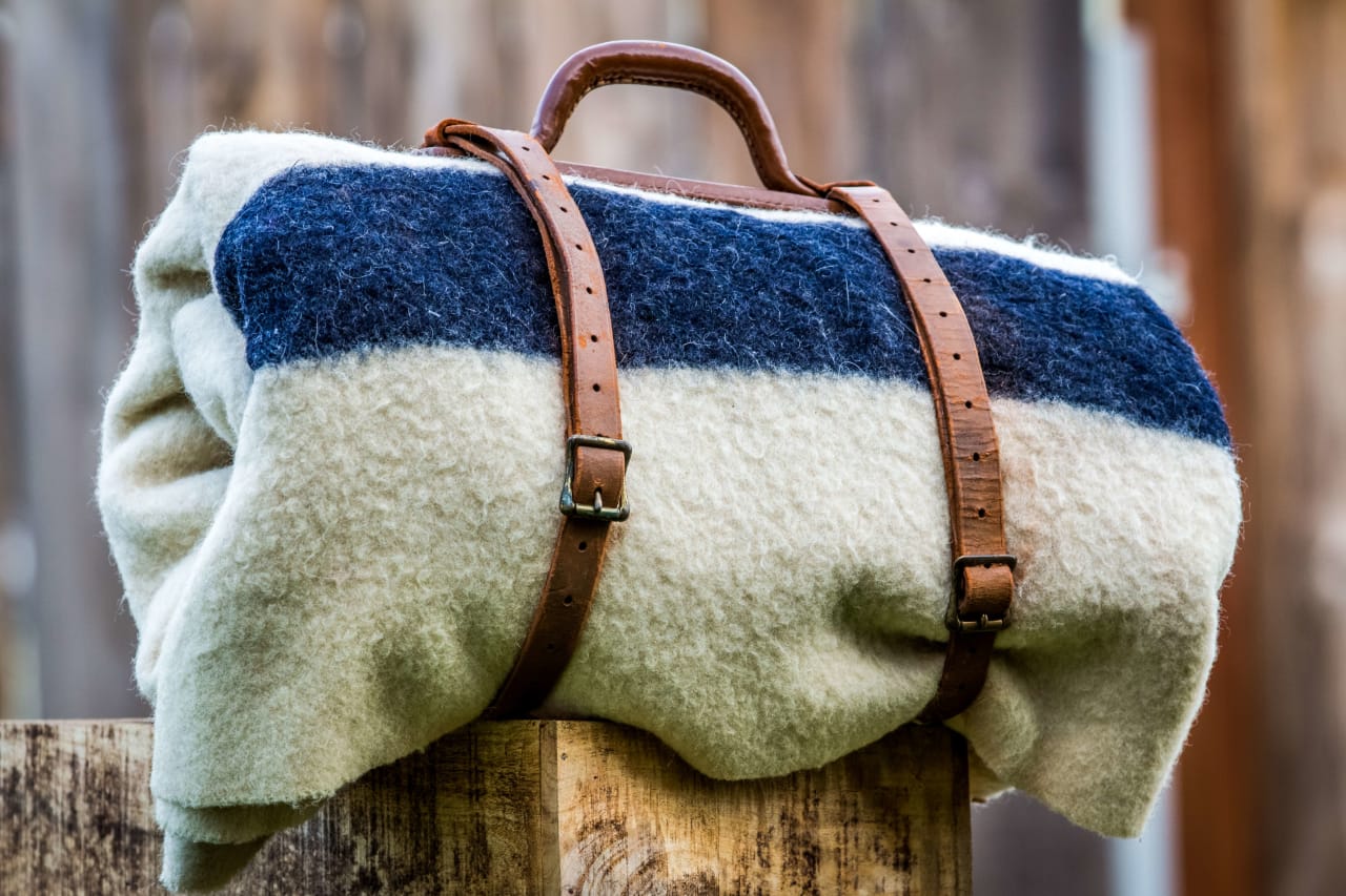 A blue and white striped blanket with leather straps wrapped around a wooden post.