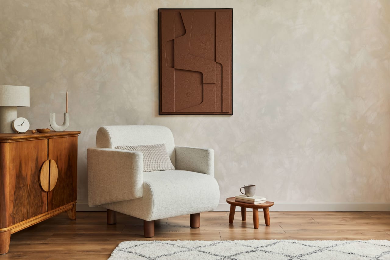 Minimalist living room with a beige armchair, wooden side table, and a textured wall hanging.