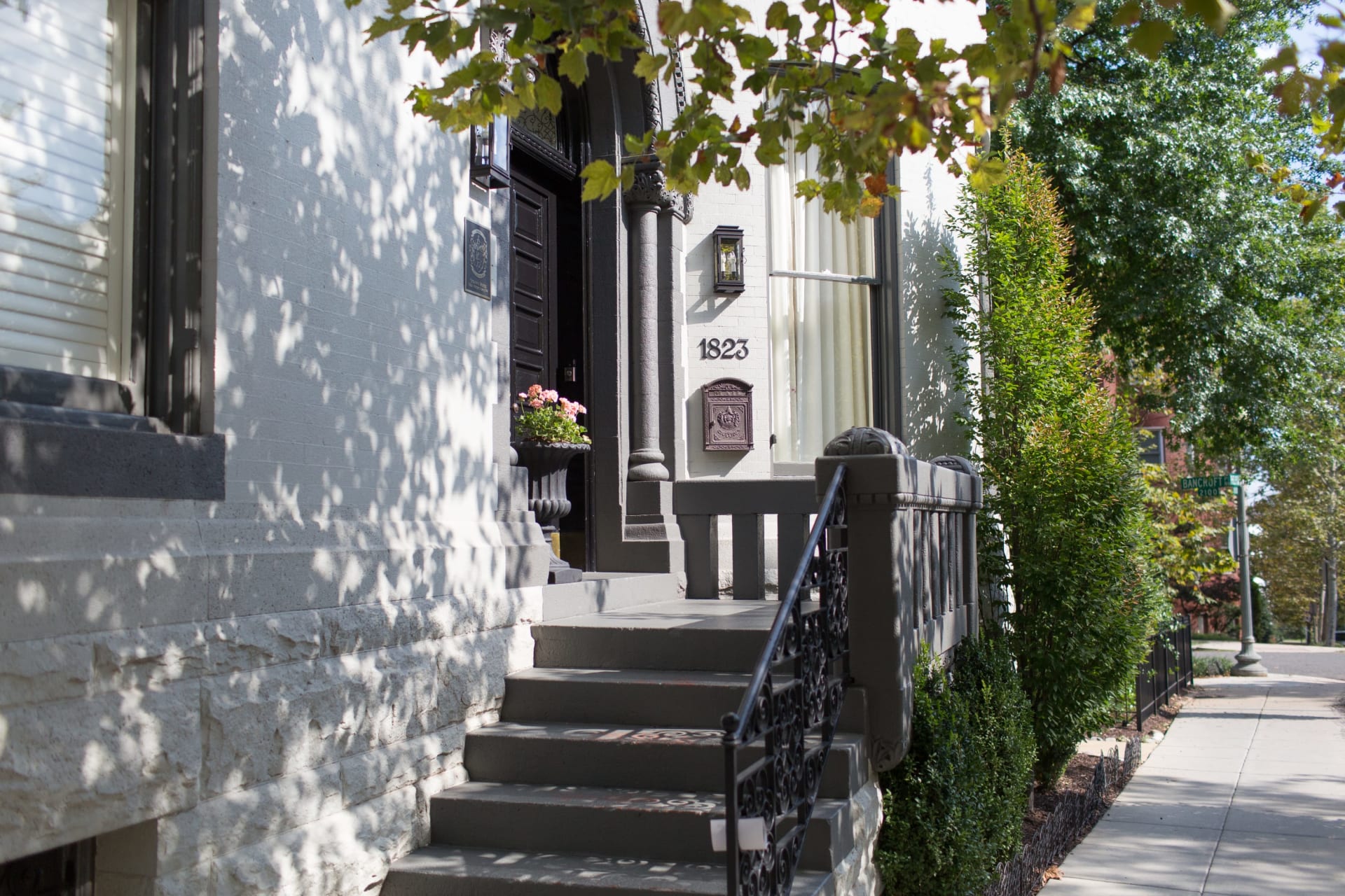 Residence entrance marked 1823, with dark steps, ornate iron railings, and leafy trees along the sidewalk.