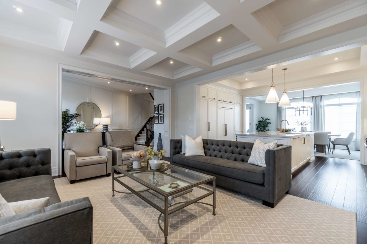 A living room with two couches, two chairs, a coffee table, and a partial view of a kitchen in the background.