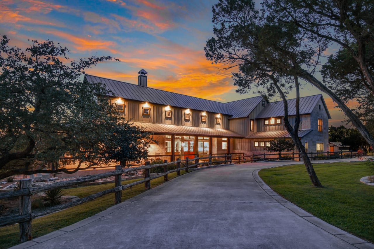 A long, paved driveway leads up to a large, barn-style house with a metal roof. 