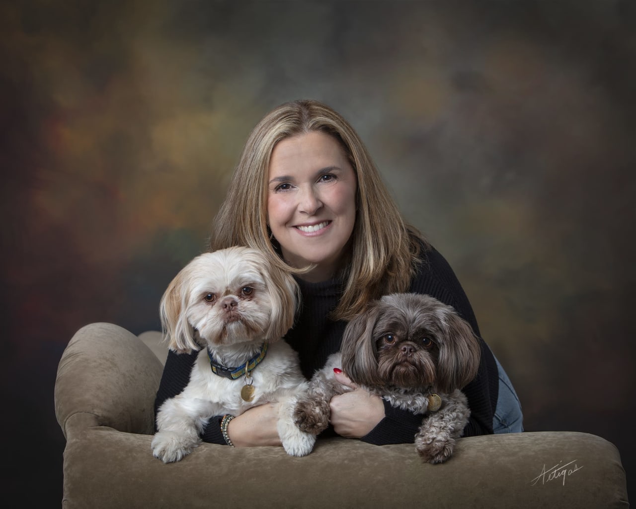 Woman smiling with two small dogs on a couch, studio backdrop.