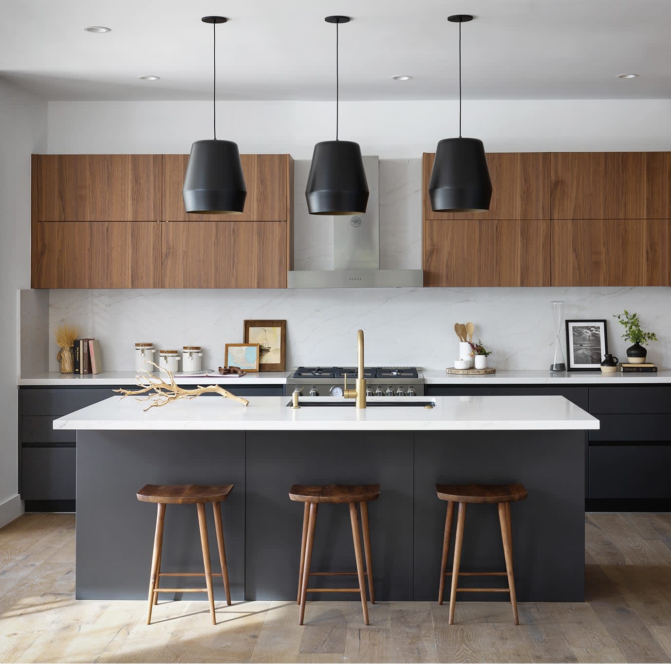 Modern kitchen with a charcoal island, warm wood cabinets, white stone counters, and three pendant lights.
