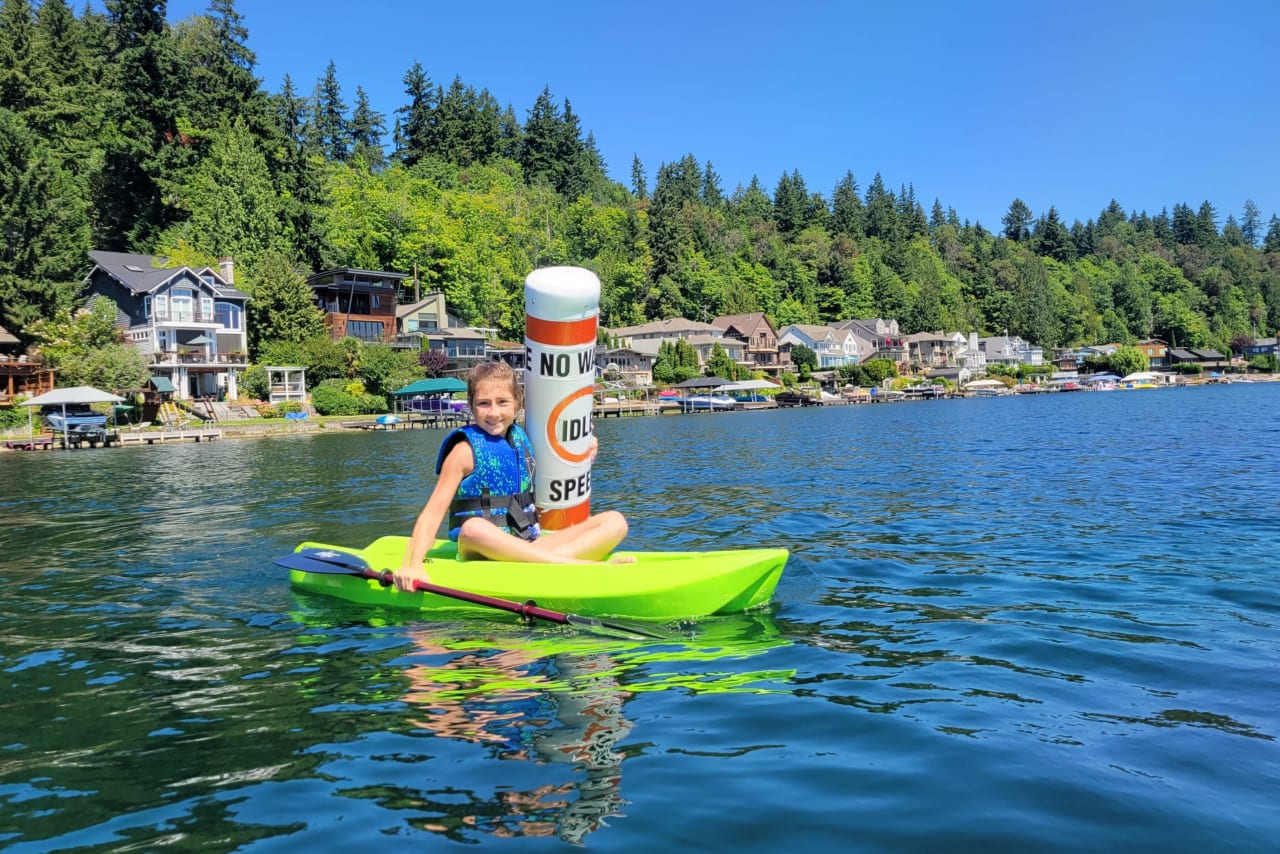 a kid riding on a green kayak holding a paddle on a lake