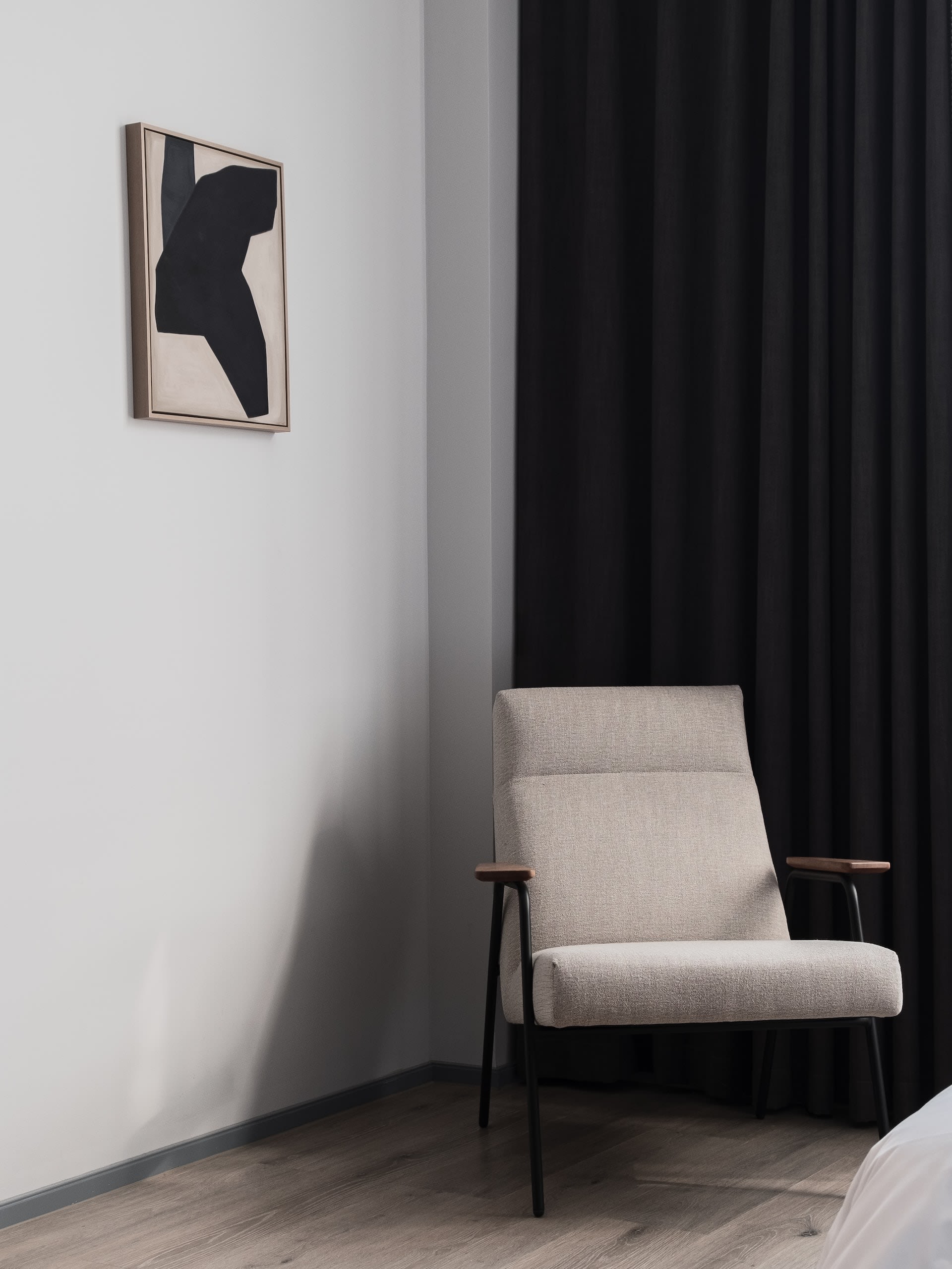 Bedroom corner with a pale armchair, dark curtains, and framed abstract art.