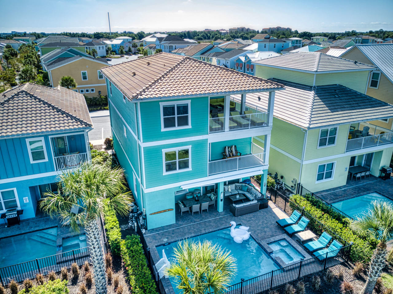 An aerial view of a house with brown roof and white exterior walls and a rectangular, blue swimming pool in the backyard.