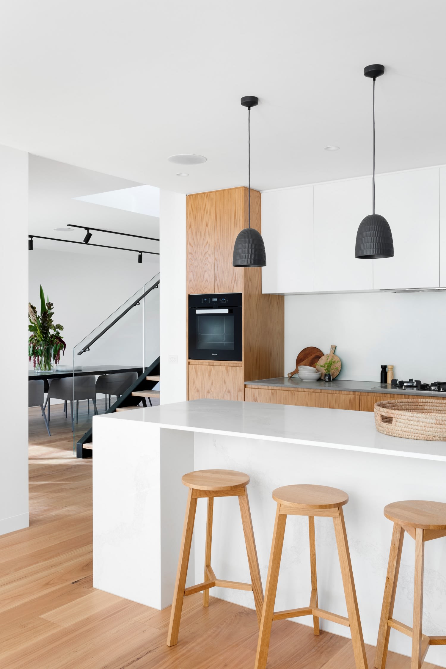  A sleek and modern Scandinavian-style kitchen features a large white kitchen island with three light wooden bar stools