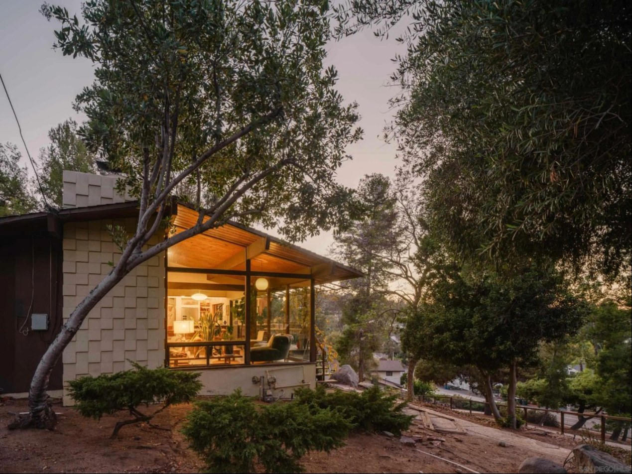 Mid-century modern home at 10923 Horizon Hills Dr, El Cajon, with a glass-walled living room glowing at dusk under mature trees