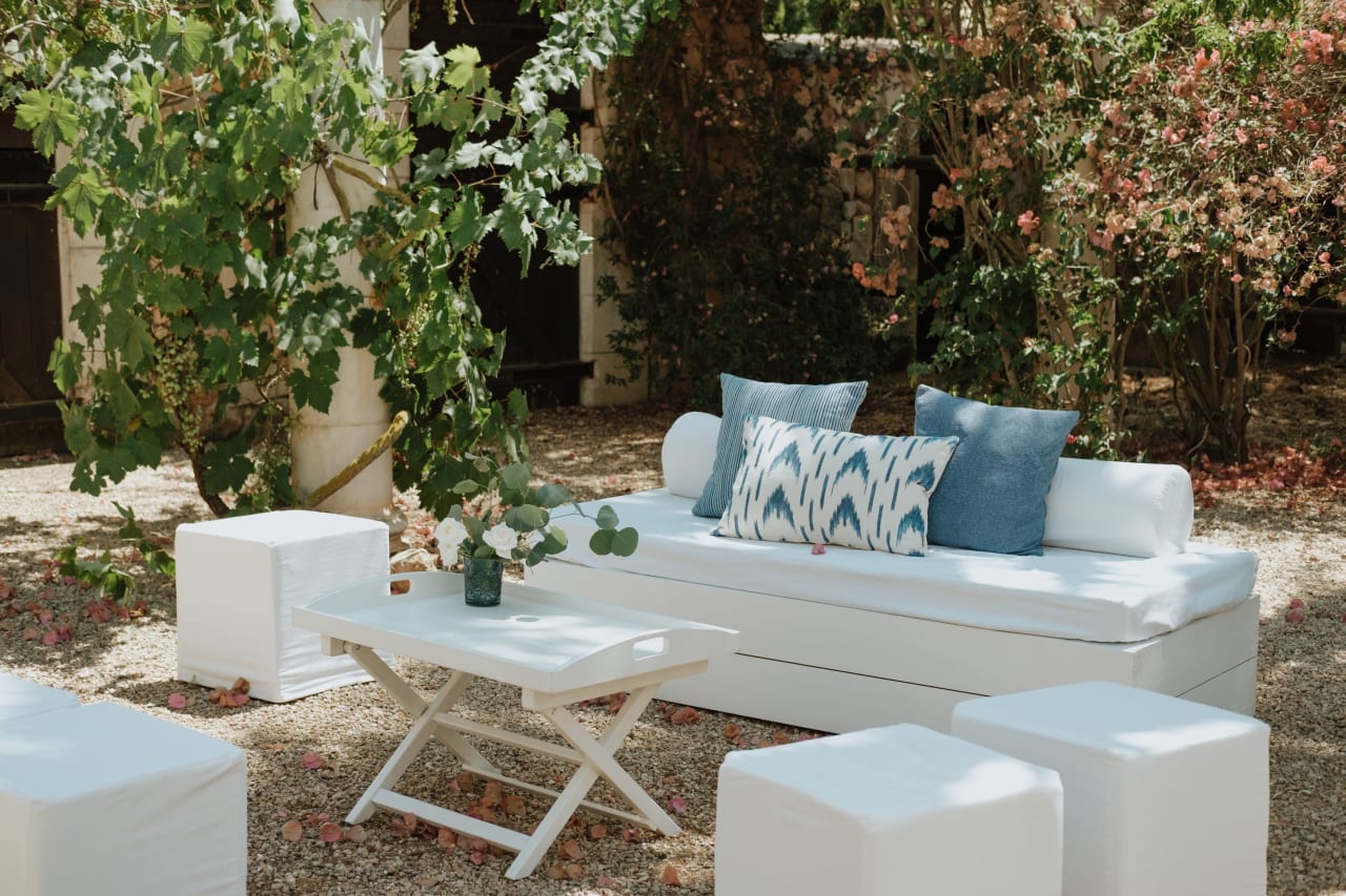 A white couch with blue throw pillows in a backyard.