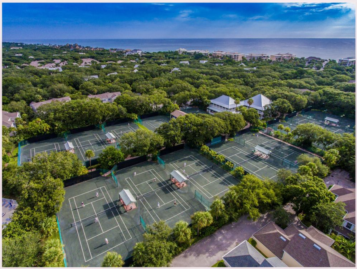 Aerial view of barrier island tennis complex with multiple clay courts, lush canopy and the Atlantic Ocean beyond