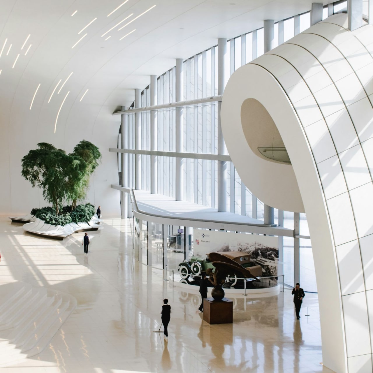 Interior view of a building with an open area, a curved white ceiling, a white centerpiece on the floor, and large windows.