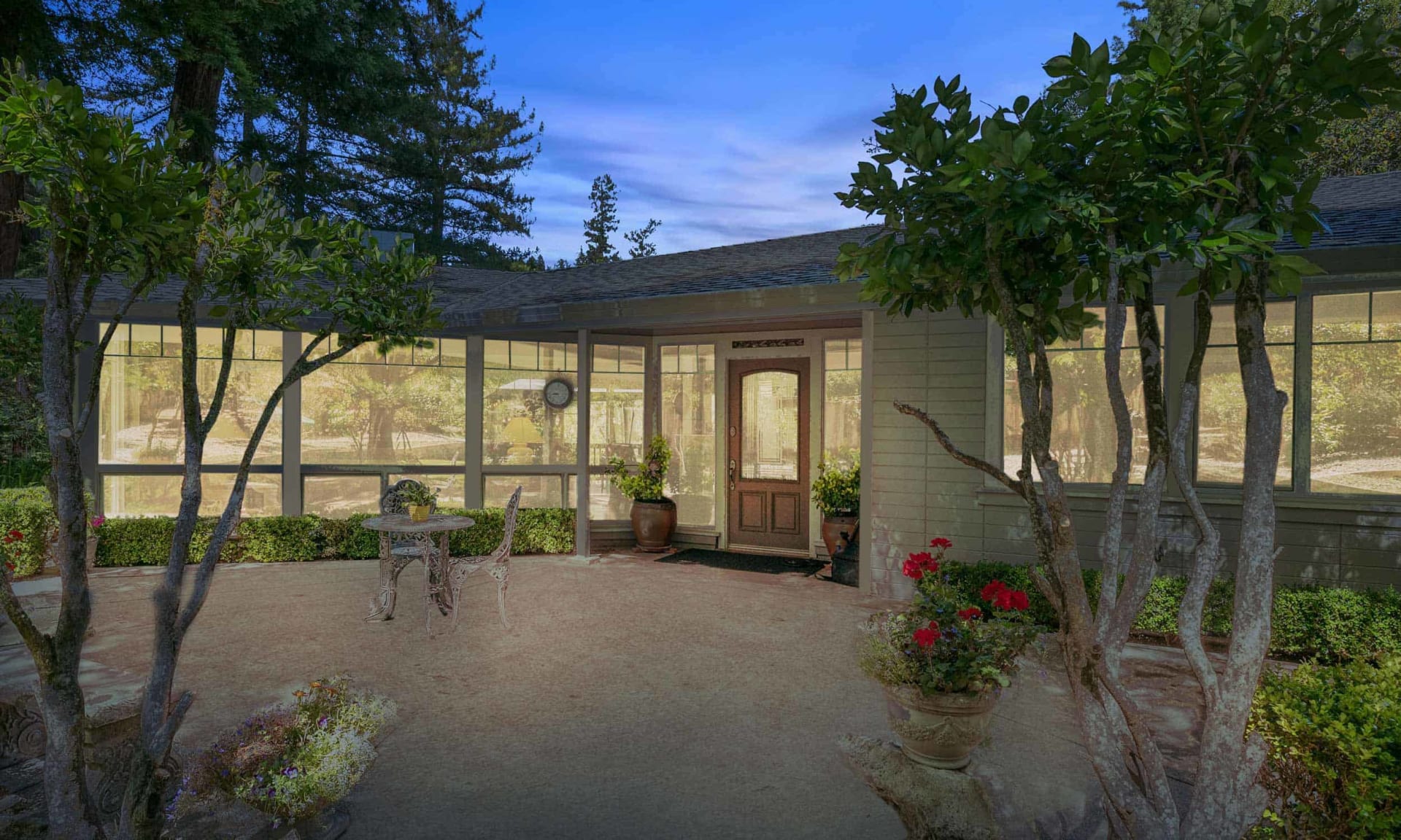 Single-story home with a wall of windows and a paved, tree-shaded entry patio.