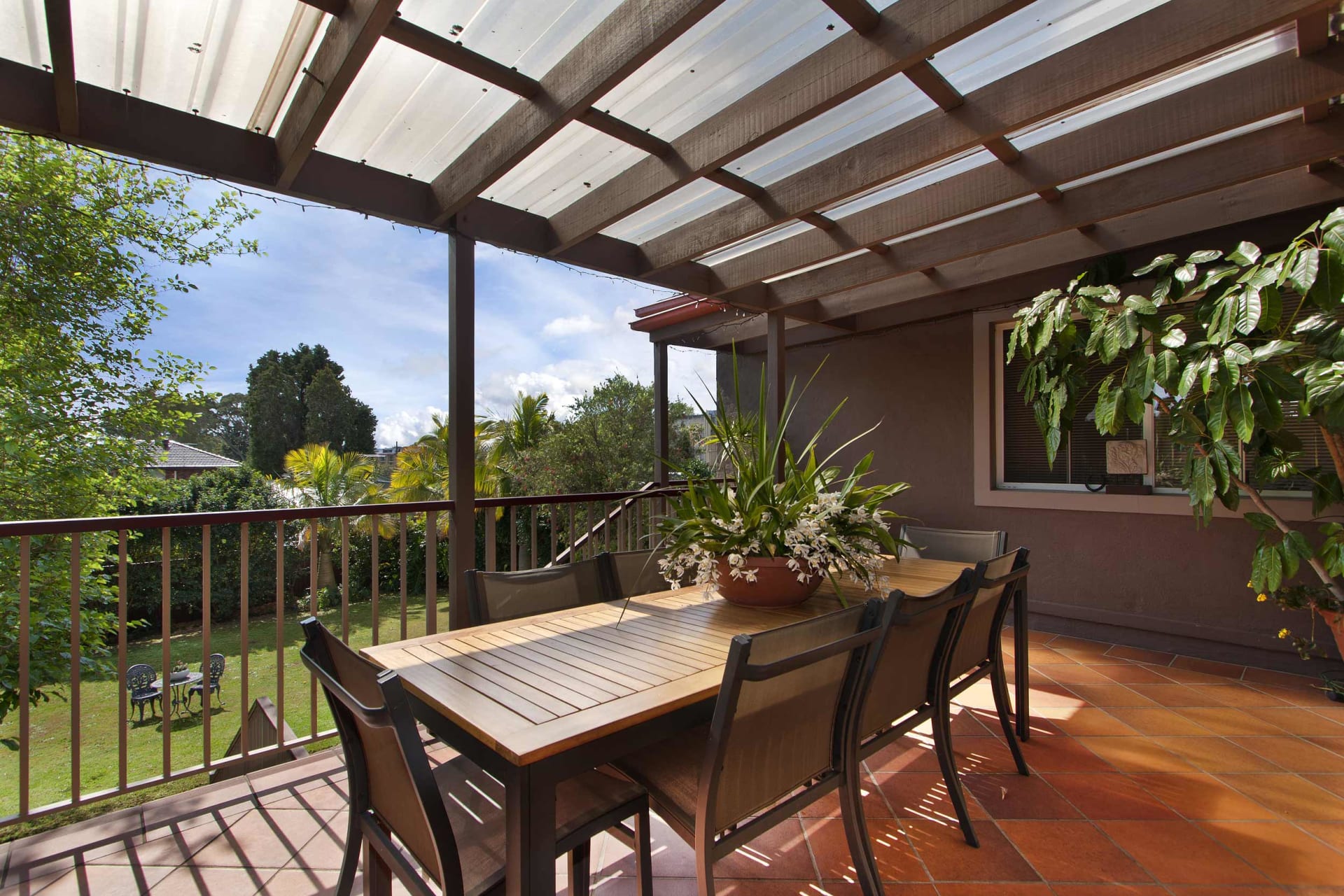 Outdoor dining patio beneath a timber pergola, with a wooden table overlooking a leafy garden.