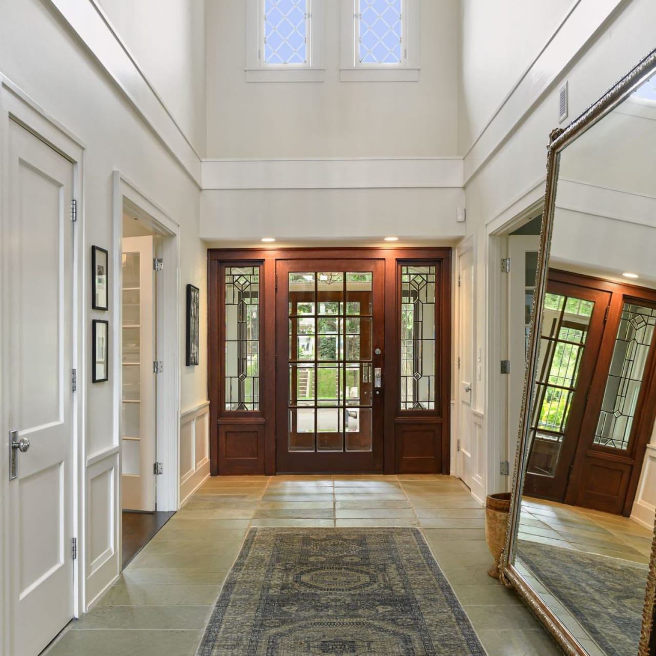 A long hallway with a large mirror on one wall and a long rectangular rug on the floor.