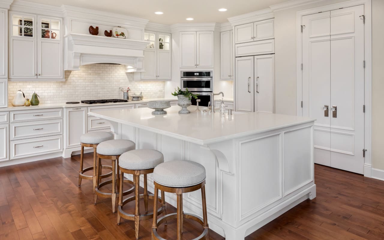 A spacious, all-white kitchen with a large island and four bar stools