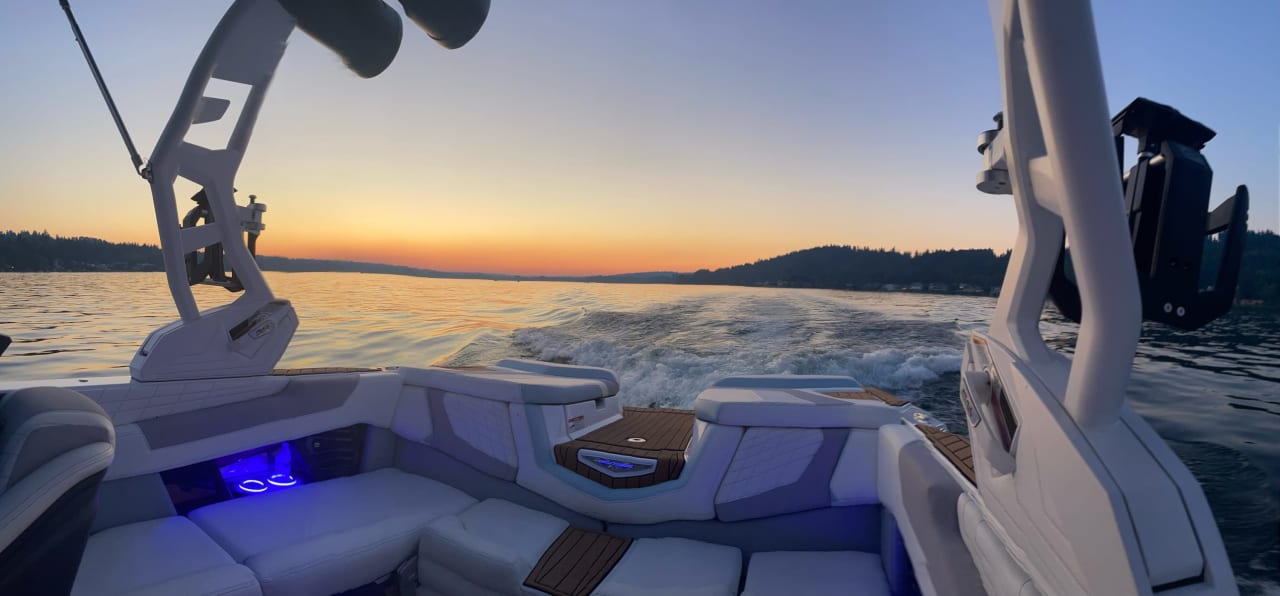 A white boat with a blue awning is floating on a lake at sunset