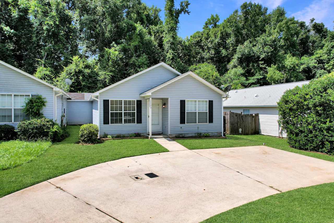 photo of front right of home from the end of the semicircle driveway featuring flowering garden beds and a large privacy hedge at 2709 Oak Park Court, Tallahassee, Florida 32308