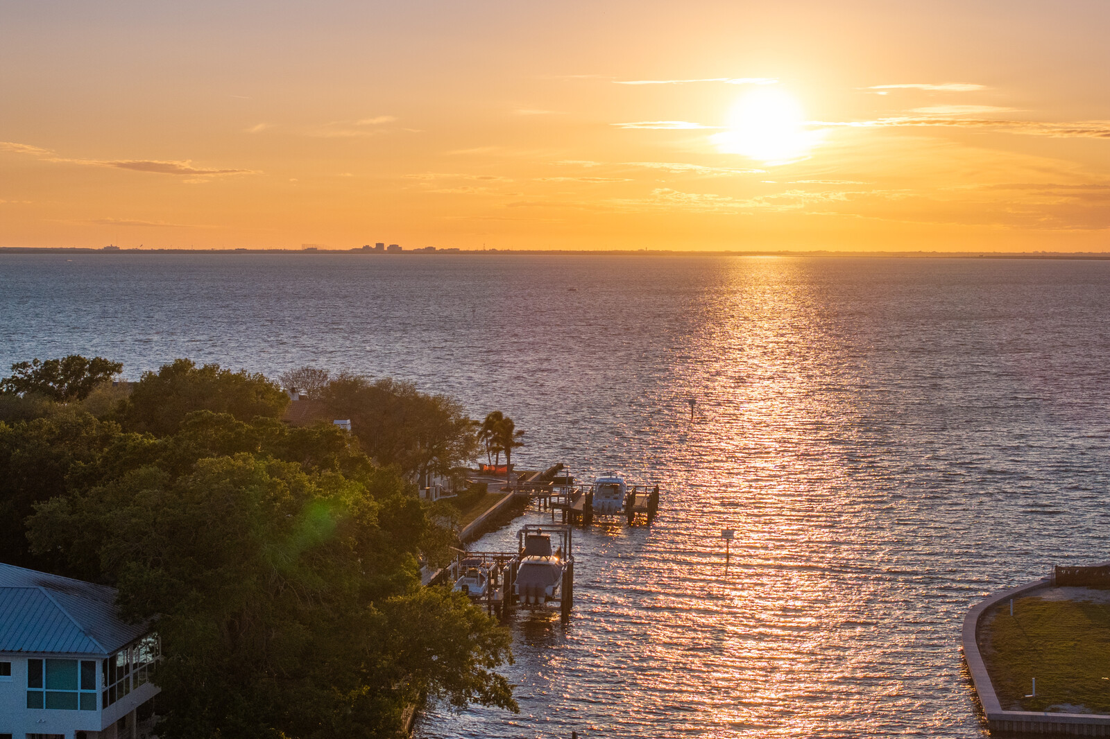 Golden sunset over Tampa Bay with private docks, boat lifts, and a waterfront home along the shoreline.