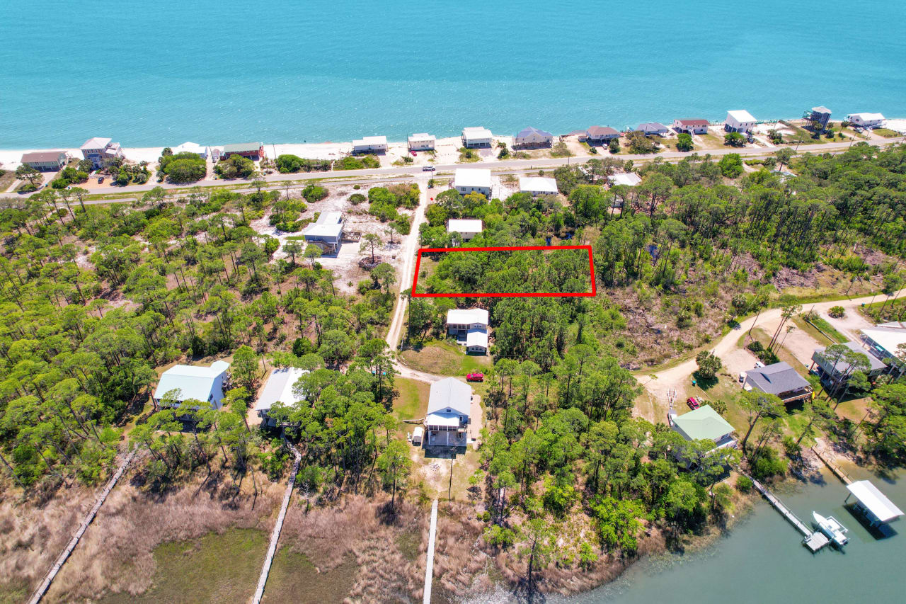 An aerial view of a residential area with a marked plot of land, showing the layout of houses and proximity to the water.