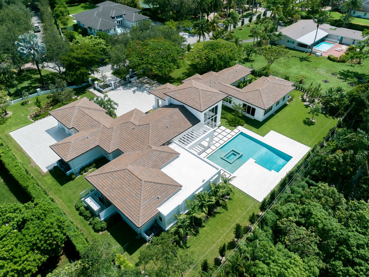 An aerial view of a large house with a rectangular swimming pool in the backyard.