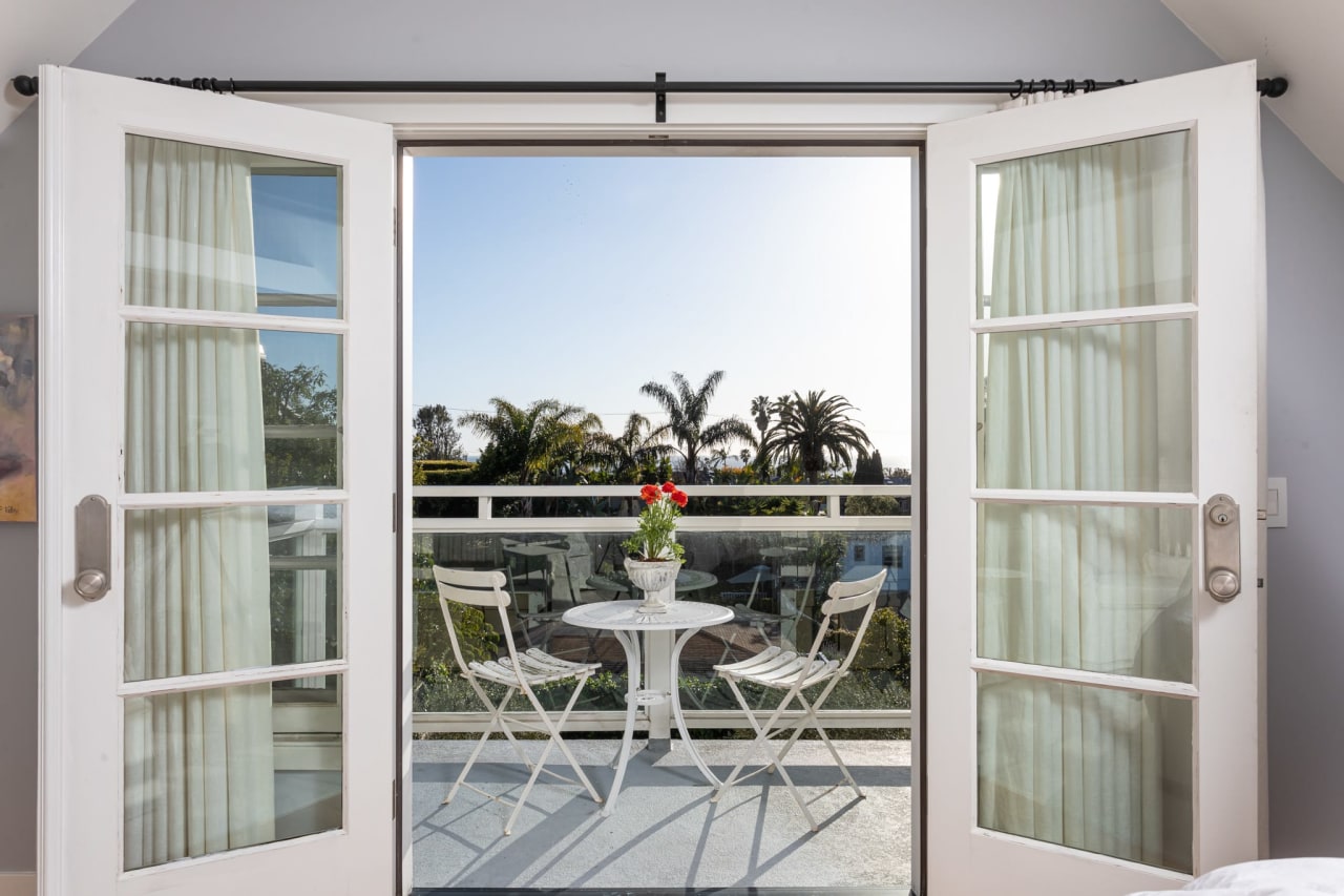 Balcony view from a luxury home with white French doors, overlooking palm trees and a sunny outdoor setting.