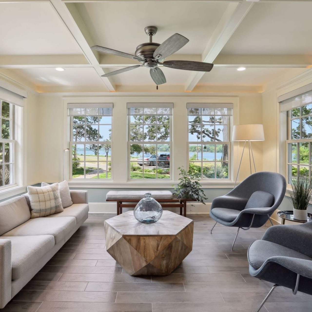 A living room with a light-colored couch, two grey armchairs, and a ceiling fan.