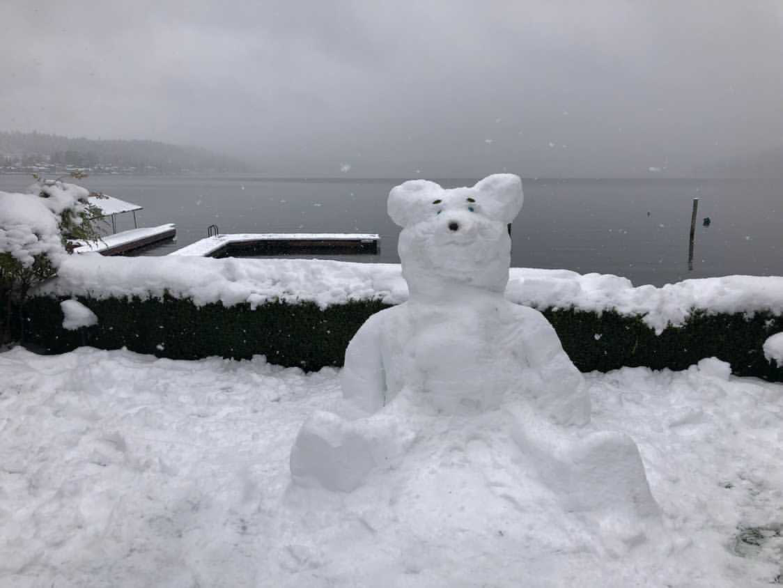 A teddy bear made out of snow in front of a lake