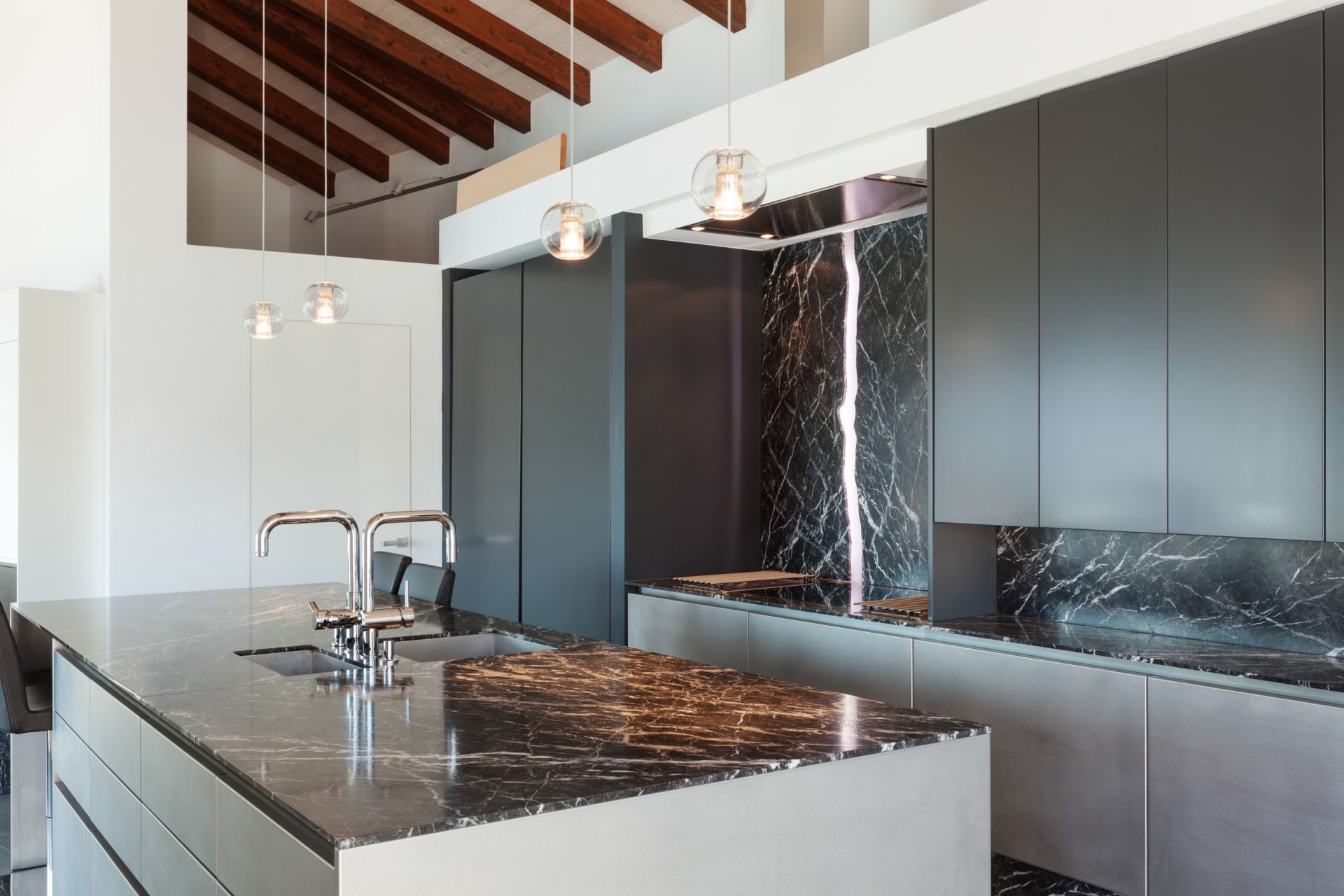  A spacious, modern kitchen with a large island featuring a dark marble countertop with prominent white and brown veining, and two stainless steel faucets.