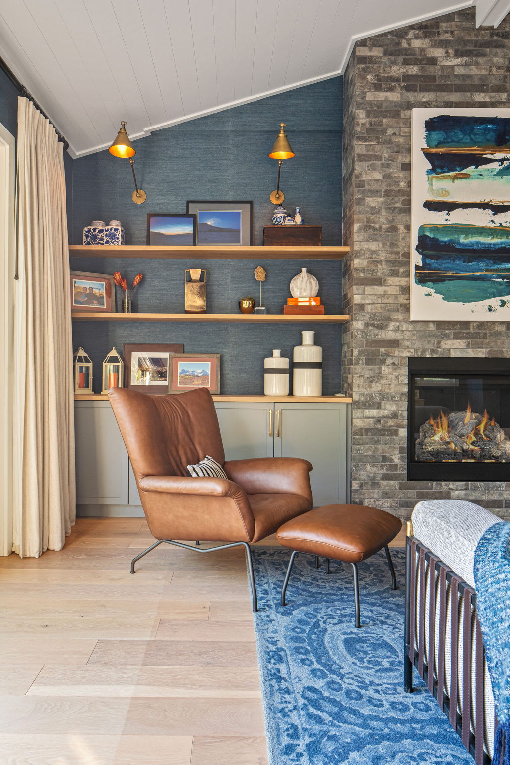 A cozy and stylish living room features a brown leather armchair with an ottoman in the foreground, resting on a vibrant blue patterned rug. 